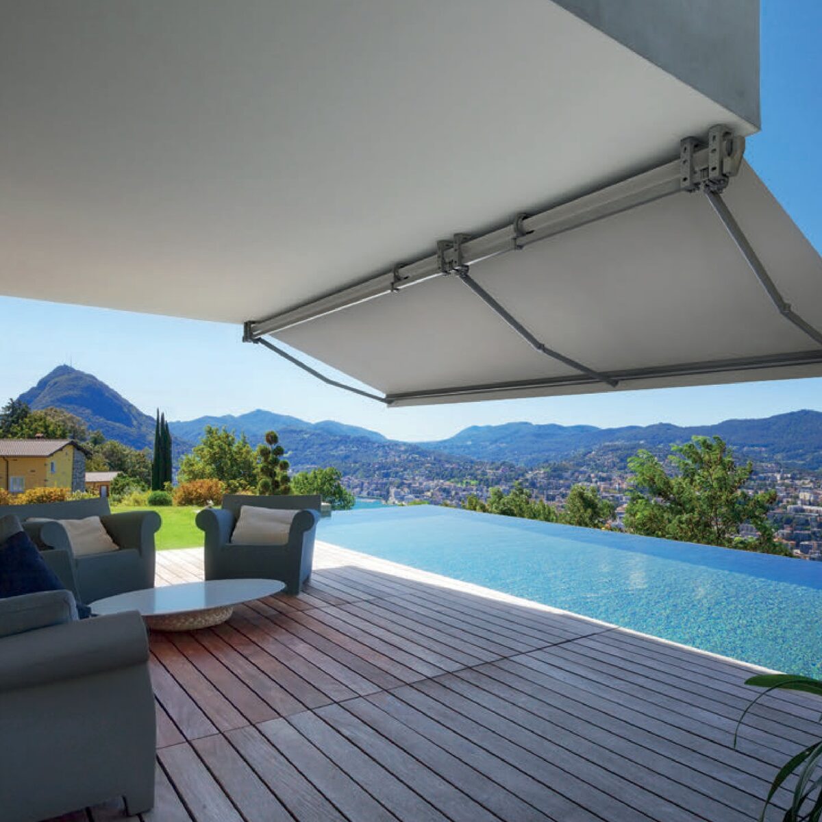 Toldo extendido sobre una terraza de madera con piscina y vistas a la montaña